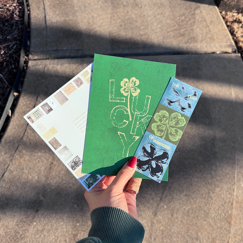 Hand holding three greeting cards with different designs on a concrete surface.